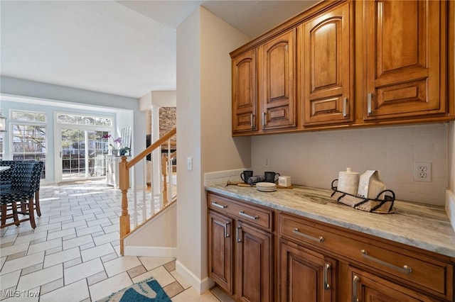 kitchen with baseboards, brown cabinets, tasteful backsplash, and light stone countertops