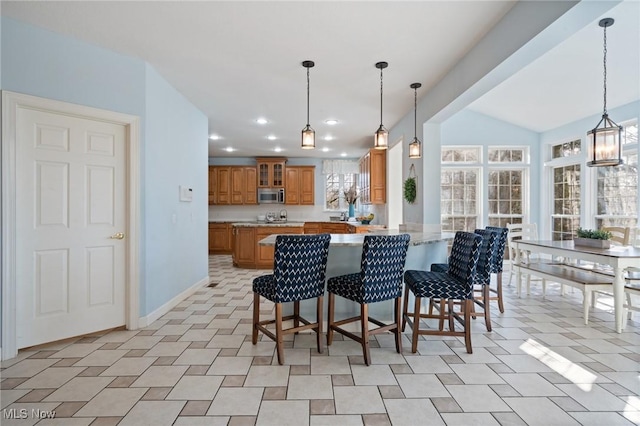 kitchen with a breakfast bar area, a peninsula, glass insert cabinets, stainless steel microwave, and brown cabinets