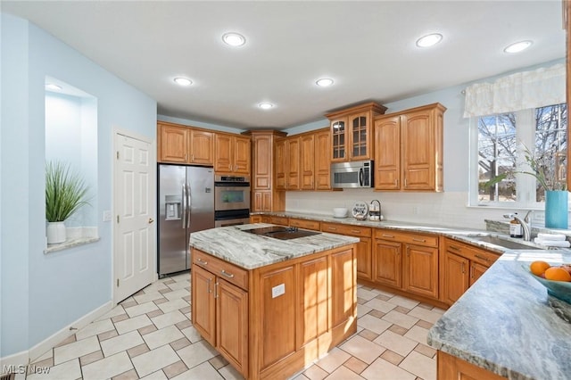 kitchen featuring a sink, stainless steel appliances, brown cabinetry, glass insert cabinets, and light stone countertops