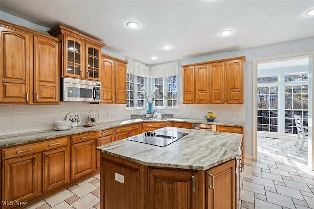 kitchen with stainless steel microwave, black electric stovetop, brown cabinetry, and light stone countertops