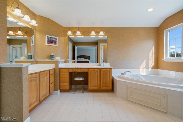 ensuite bathroom featuring two vanities, a bath, a stall shower, and a sink