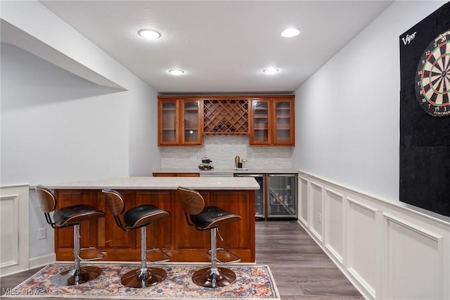 bar featuring dark wood-style floors, indoor wet bar, wine cooler, a decorative wall, and tasteful backsplash