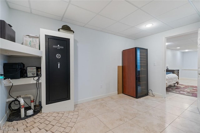 interior space featuring light tile patterned flooring, a drop ceiling, and baseboards