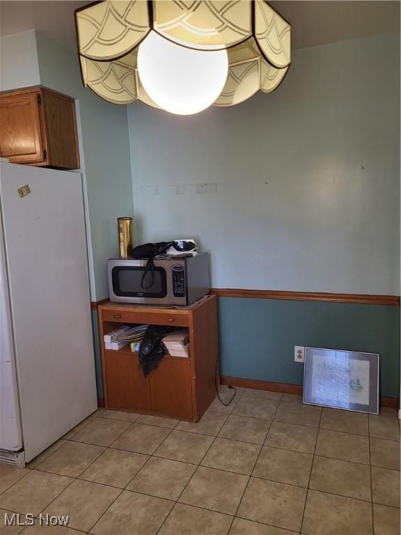 kitchen featuring light tile patterned floors, stainless steel microwave, brown cabinetry, and freestanding refrigerator