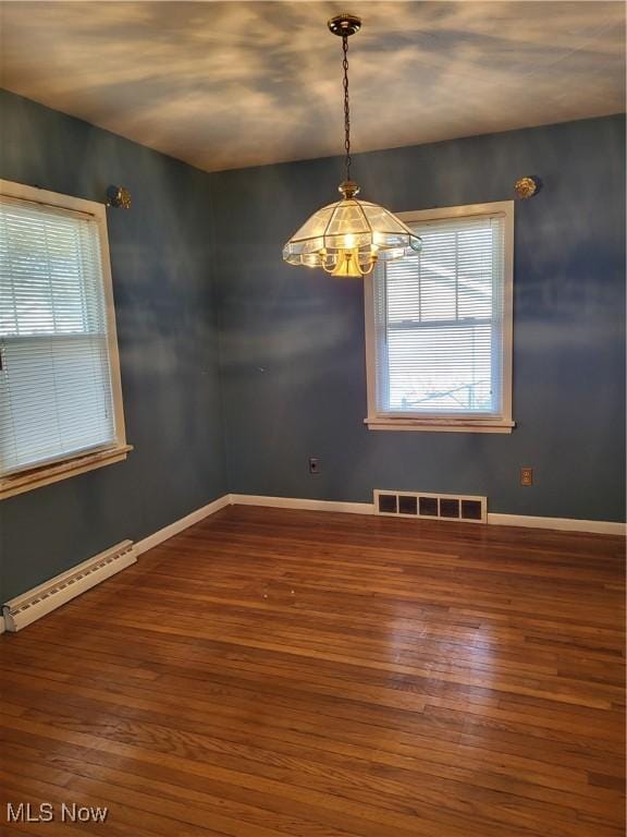 empty room with visible vents, baseboard heating, a healthy amount of sunlight, and wood finished floors