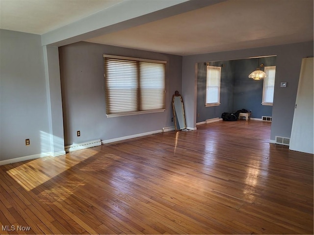 unfurnished room featuring hardwood / wood-style floors, visible vents, baseboards, and a baseboard heating unit