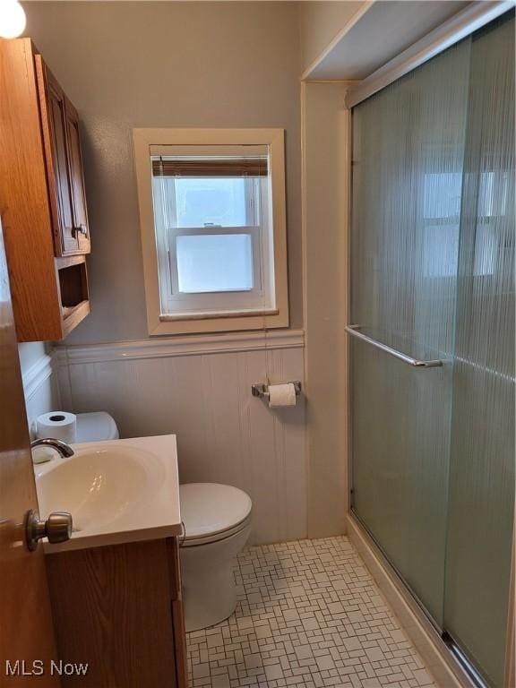 bathroom with a shower with door, a wainscoted wall, toilet, and vanity