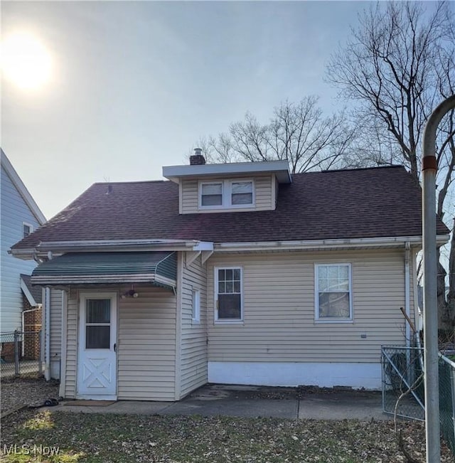 rear view of property with a chimney, roof with shingles, and fence