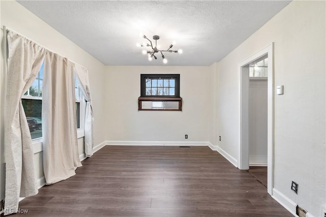 spare room featuring baseboards, a notable chandelier, dark wood-style flooring, and a textured ceiling