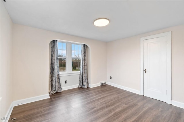 empty room featuring visible vents, wood finished floors, and baseboards