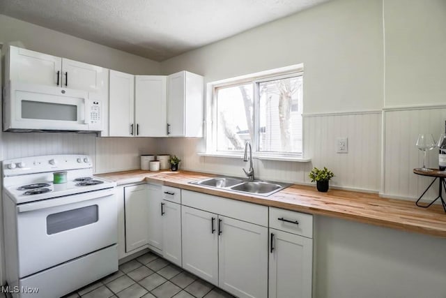 kitchen with butcher block countertops, wainscoting, white appliances, white cabinetry, and a sink