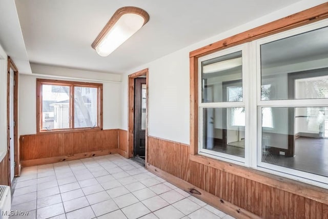 unfurnished room with light tile patterned floors, a wainscoted wall, and wood walls