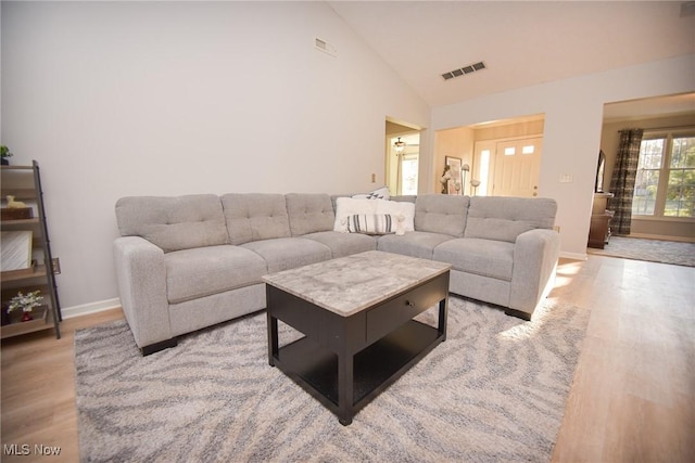 living room featuring high vaulted ceiling, light wood-style floors, visible vents, and baseboards