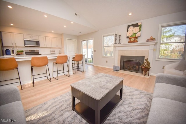 living room featuring visible vents, a fireplace with flush hearth, vaulted ceiling, recessed lighting, and light wood-style flooring