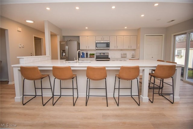 kitchen featuring light wood finished floors, a breakfast bar area, decorative backsplash, stainless steel appliances, and a sink