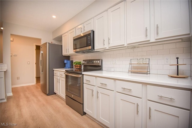 kitchen featuring tasteful backsplash, white cabinetry, stainless steel appliances, light wood-style floors, and light countertops