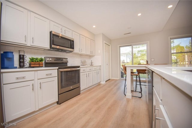 kitchen with stainless steel appliances, light wood finished floors, backsplash, and white cabinetry