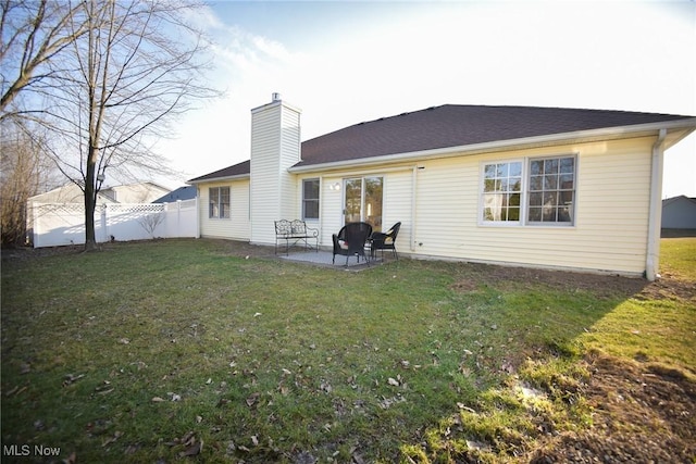 rear view of house with a patio, a chimney, a yard, and fence