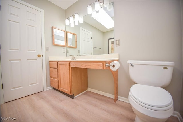 bathroom with toilet, vanity, baseboards, and wood finished floors