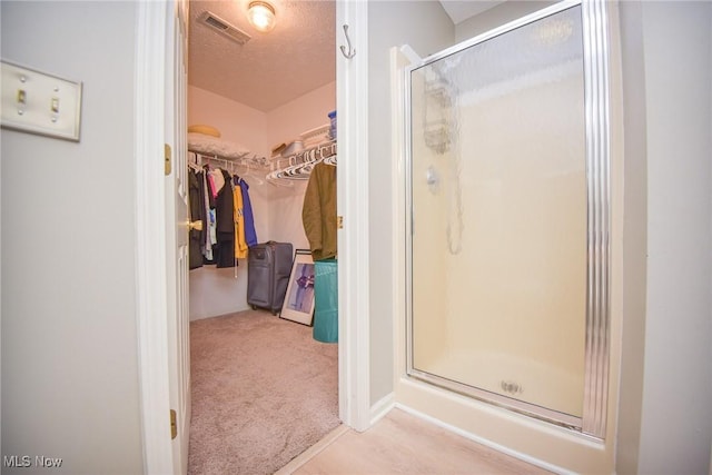 bathroom featuring a walk in closet, visible vents, a stall shower, and a textured ceiling