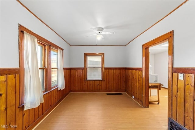 unfurnished room with light wood-type flooring, visible vents, ornamental molding, wooden walls, and wainscoting