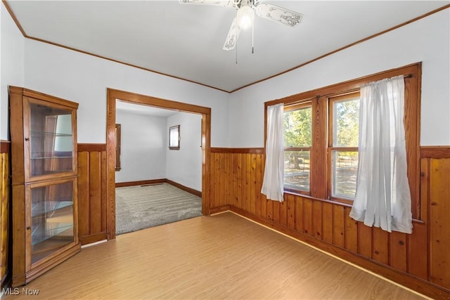 unfurnished room featuring wooden walls, crown molding, wainscoting, and light wood finished floors