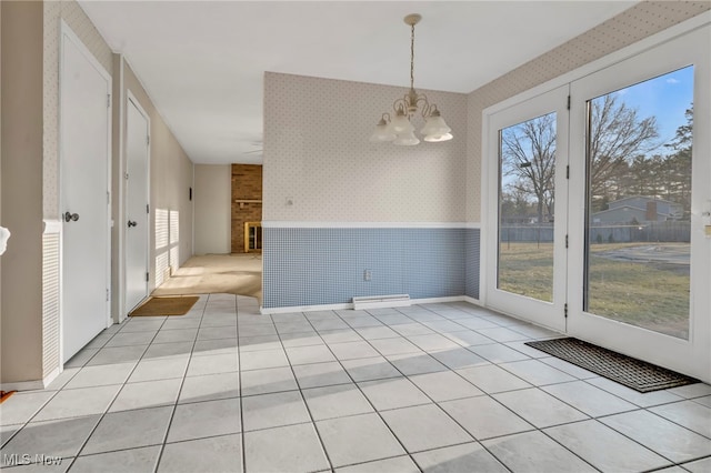 unfurnished room with wallpapered walls, light tile patterned floors, a wainscoted wall, and a chandelier