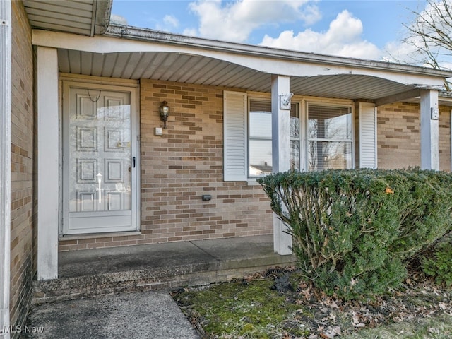 view of exterior entry with brick siding and covered porch