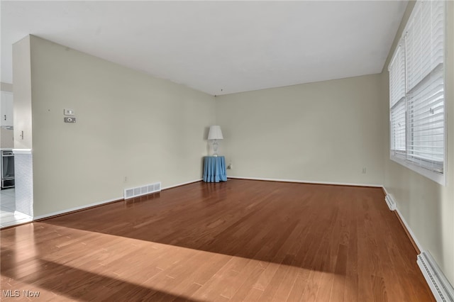 unfurnished room featuring baseboard heating, baseboards, visible vents, and wood finished floors