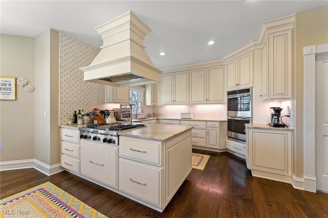 kitchen with premium range hood, cream cabinets, dark wood-style floors, stainless steel appliances, and a sink