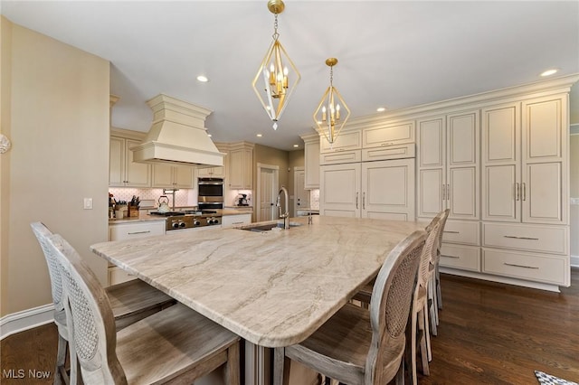 kitchen featuring a sink, custom exhaust hood, cream cabinetry, and dark wood-style floors