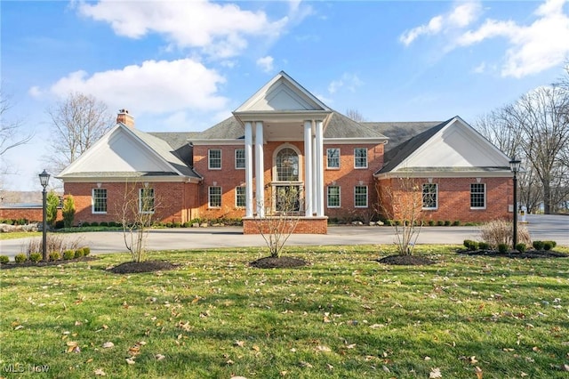 greek revival inspired property with brick siding, a chimney, and a front yard