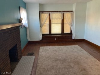 unfurnished living room with visible vents, a brick fireplace, baseboards, and wood finished floors