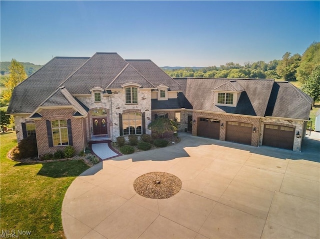 french country home featuring brick siding, concrete driveway, a front yard, a garage, and stone siding