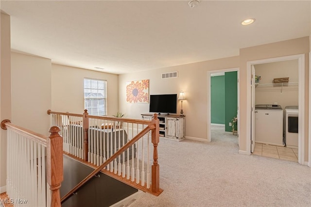 hall with visible vents, an upstairs landing, carpet flooring, and washer and clothes dryer