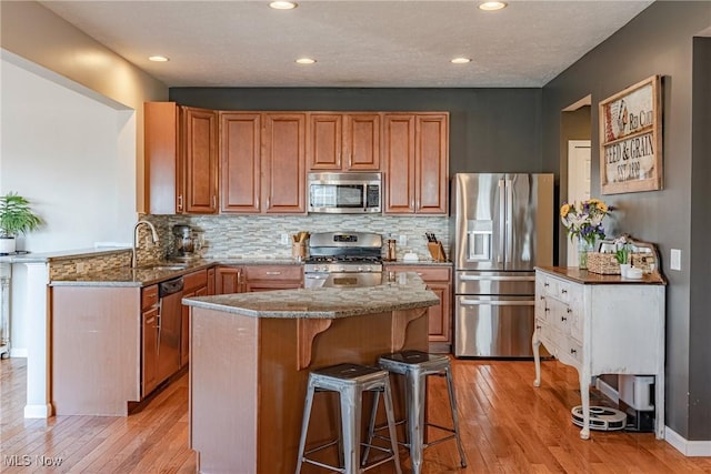 kitchen with a breakfast bar area, stone countertops, a sink, stainless steel appliances, and light wood-style floors