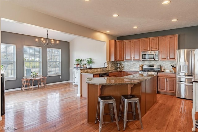 kitchen with dark stone countertops, light wood-style flooring, a sink, stainless steel appliances, and tasteful backsplash