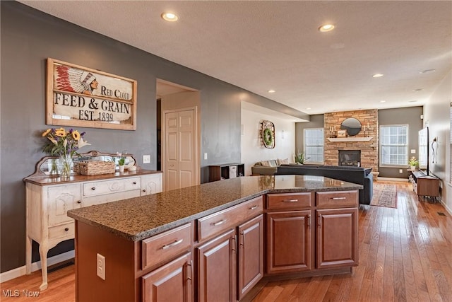 kitchen featuring baseboards, a stone fireplace, a kitchen island, and light wood-style floors