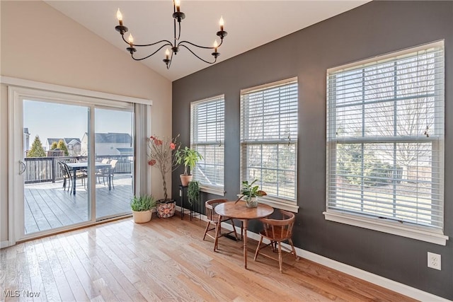 dining space with a wealth of natural light, a notable chandelier, light wood-type flooring, and vaulted ceiling