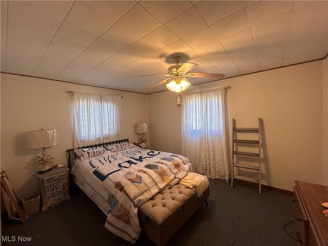 bedroom with dark colored carpet, multiple windows, and a ceiling fan