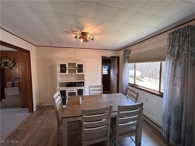 dining area with a baseboard heating unit, crown molding, wood finished floors, and baseboards