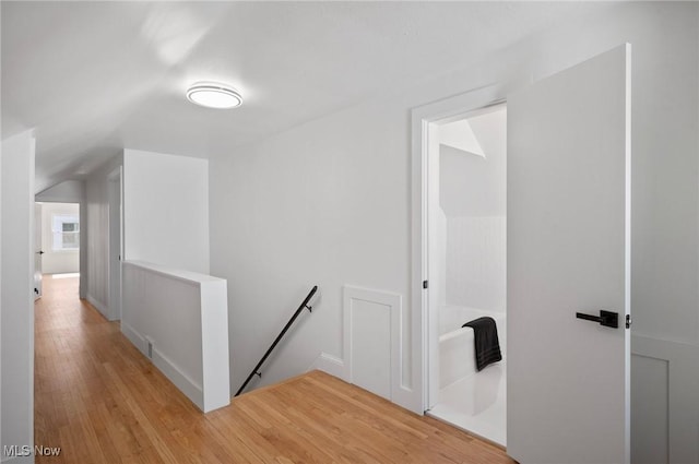 corridor featuring light wood-type flooring, an upstairs landing, and vaulted ceiling