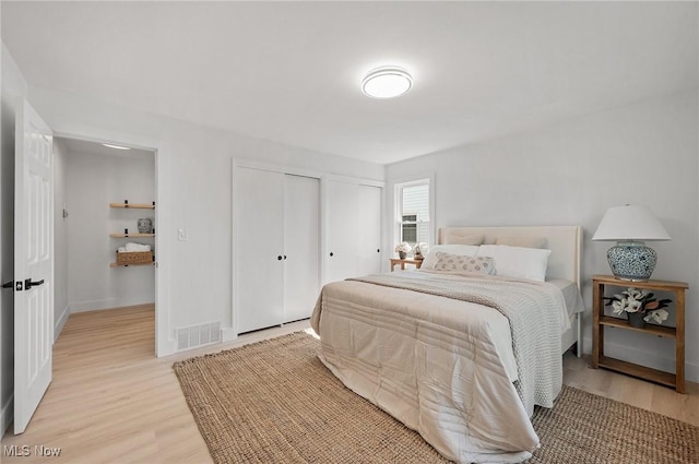 bedroom with baseboards, visible vents, light wood finished floors, and multiple closets