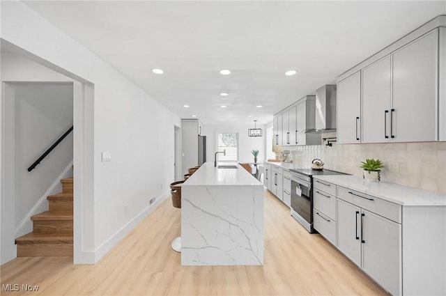 kitchen featuring tasteful backsplash, stainless steel range with electric cooktop, light wood-style floors, wall chimney exhaust hood, and a sink