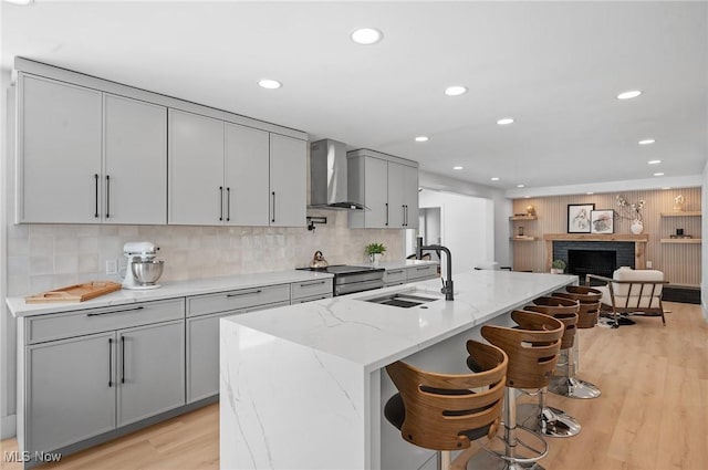 kitchen with wall chimney range hood, stainless steel electric range oven, light wood-type flooring, gray cabinets, and a sink