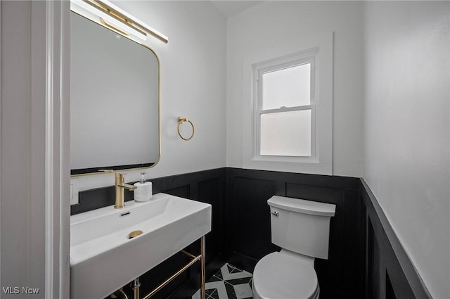 bathroom with vanity, a decorative wall, toilet, and wainscoting