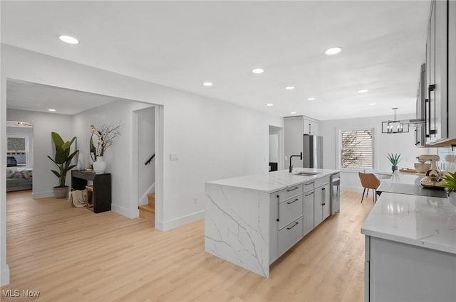 kitchen with gray cabinetry, a kitchen island with sink, a sink, stainless steel appliances, and light wood-style floors