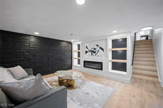 living room featuring built in features, stairs, recessed lighting, wood finished floors, and a glass covered fireplace