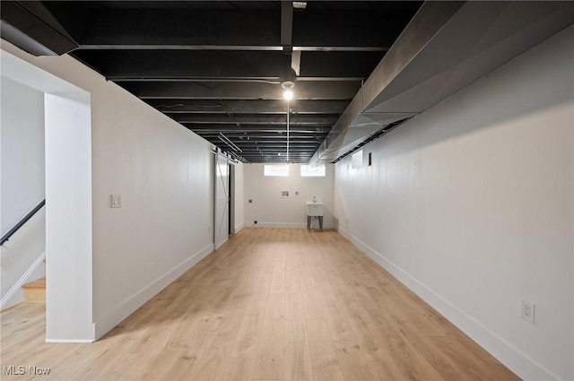 below grade area featuring a sink, stairway, baseboards, and light wood-style flooring