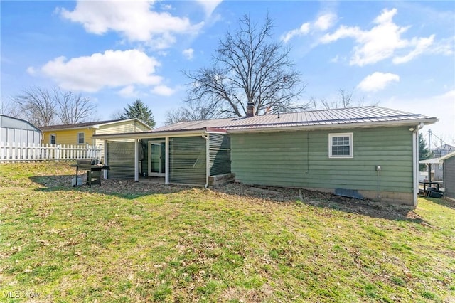 back of property featuring a chimney, a lawn, metal roof, and fence